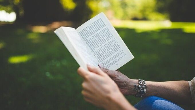 Un livre ouvert, dans un jardin, tenu par une personne.